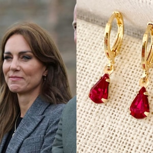 May include: A pair of gold hoop earrings with a dangling teardrop-shaped ruby red gemstone.