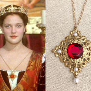 May include: A gold pendant necklace with a large, round, red gemstone. The ornate, filigree setting is decorated with small, white pearls. The necklace is displayed against a neutral background.
