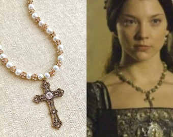 May include: A gold cross pendant necklace with a pearl and crystal beaded chain. The cross has a detailed design and a clear crystal in the center.