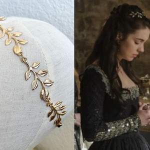 May include: A gold-colored leaf-shaped headband. The leaves are connected by delicate chains. The headband is displayed on a white mannequin head. The second image shows a woman wearing a similar headband.