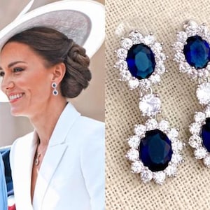 May include: Elegant silver earrings featuring large, oval, deep blue gemstones surrounded by a halo of smaller, clear stones. The earrings have a dangling design with a second, smaller clear stone between the blue gems. A classic jewelry piece.
