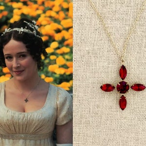 May include: A gold chain necklace with a pendant featuring a red crystal cross. The cross is made up of five red crystals in a cross shape.