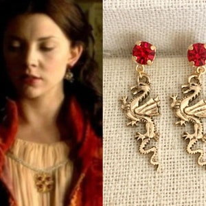 May include: Gold dragon earrings with red crystal accents. The dragons are detailed and have a textured finish.