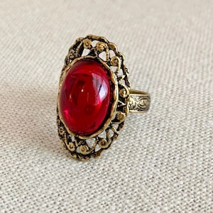May include: A gold ring with an oval-shaped red gemstone set in a filigree design.