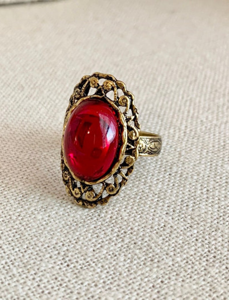 May include: A gold ring with an oval-shaped red gemstone set in a filigree design.