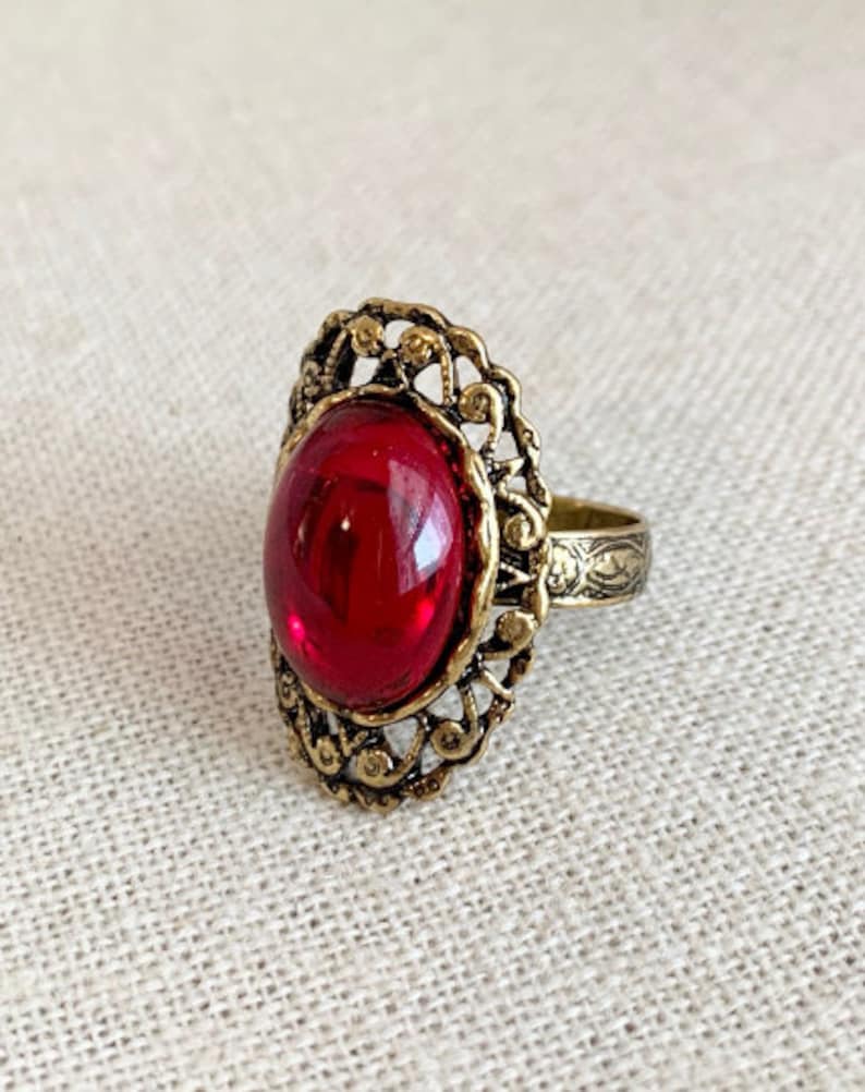 May include: A gold ring with an ornate design and a large, oval-shaped, red gemstone.