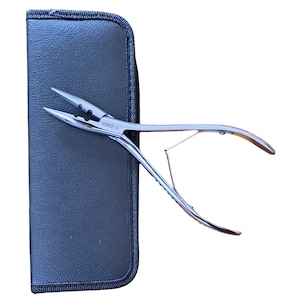 May include: Silver-coloured pliers with pointed tips, next to a black, zipped case. The pliers have a curved handle and a small, spring-like mechanism. The case is rectangular with a stitched border.