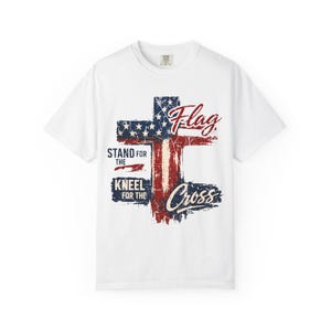 Puede incluir: Camiseta blanca con un dise&ntilde;o desgastado de una cruz con los colores de la bandera estadounidense. Las palabras "Flag", "Stand for the", "Kneel for the" y "Cross" est&aacute;n impresas.
