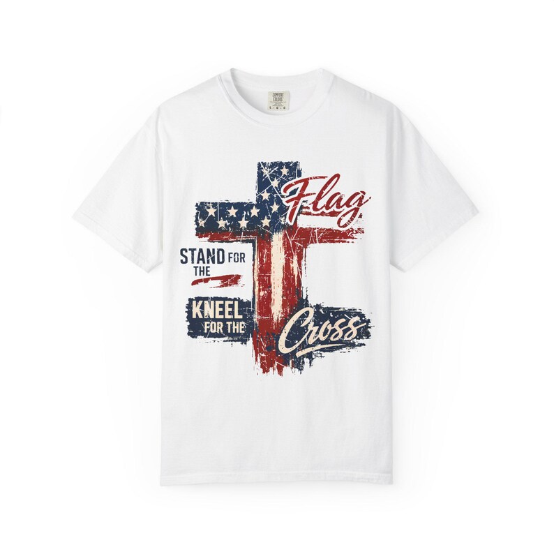 Puede incluir: Camiseta blanca con un dise&ntilde;o desgastado de una cruz con los colores de la bandera estadounidense. Las palabras "Flag", "Stand for the", "Kneel for the" y "Cross" est&aacute;n impresas.