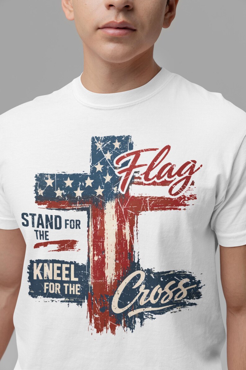 Puede incluir: Camiseta blanca con un dise&ntilde;o de cruz desgastada en los colores de la bandera americana. El dise&ntilde;o incluye la palabra "Flag" y las frases "Stand for the" y "Kneel for the Cross."