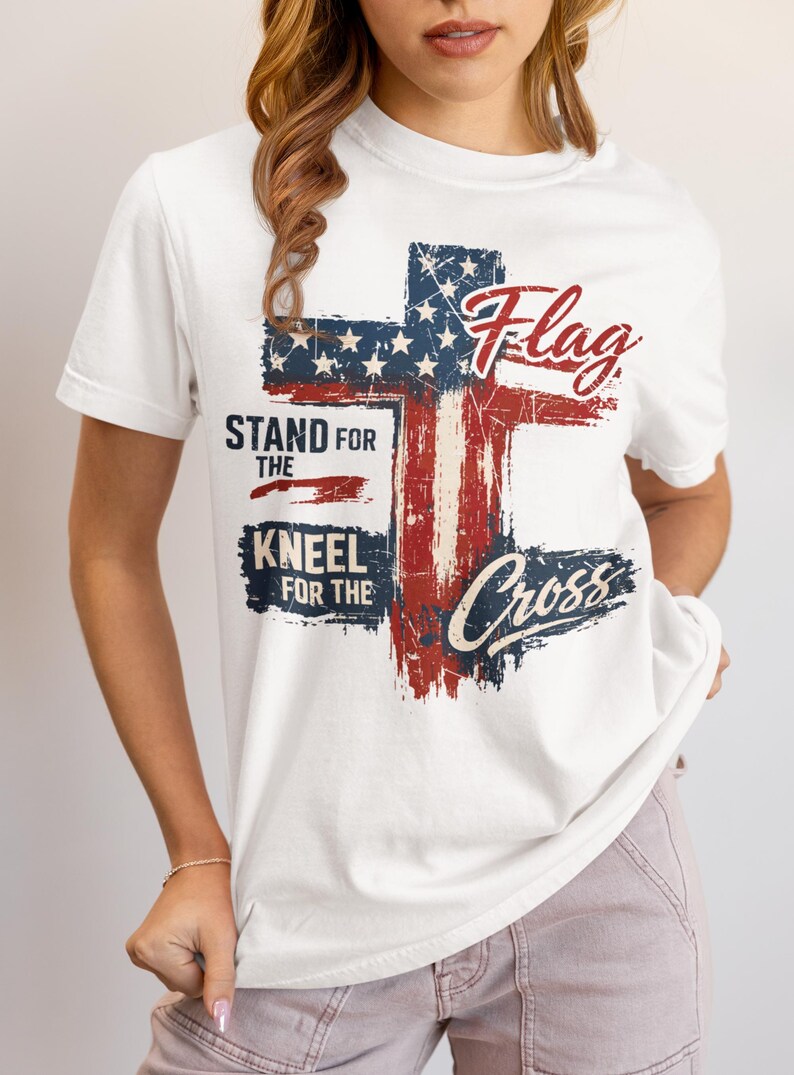 Puede incluir: Camiseta blanca con un dise&ntilde;o de cruz de la bandera estadounidense desgastada. La camiseta incluye las palabras "Flag" y "Cross" en escritura cursiva, junto con "Stand for the" y "Kneel for the".