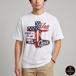 Puede incluir: Camiseta blanca con un dise&ntilde;o de cruz de la bandera estadounidense desgastada. El dise&ntilde;o incorpora elementos rojos y azules con las palabras "Flag", "Stand for the", "Kneel for the" y "Cross".