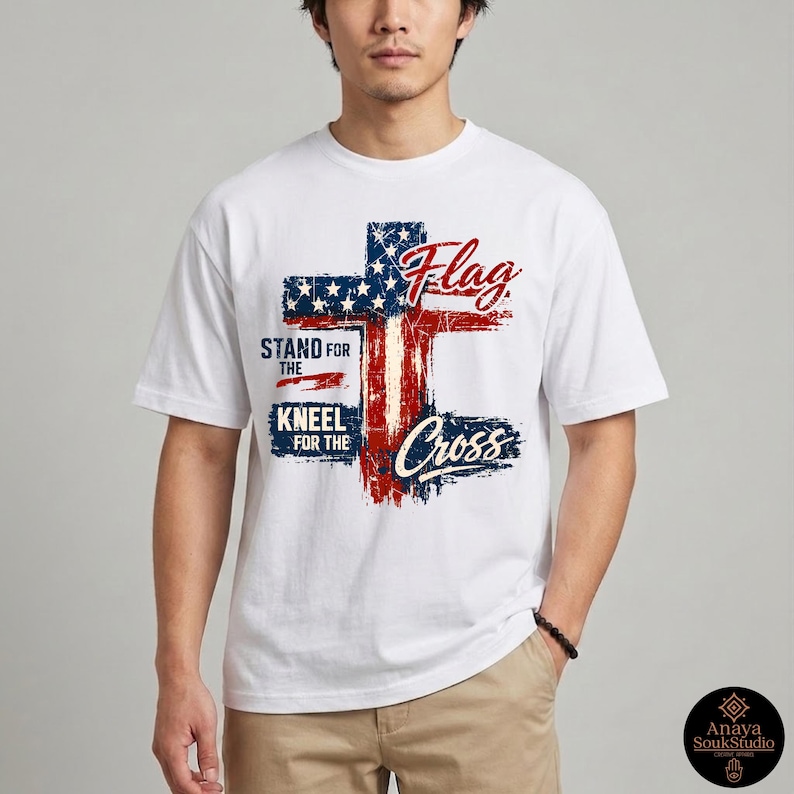 May include: White t-shirt featuring a distressed American flag cross design. The design incorporates red and blue elements with the words "Flag", "Stand for the", "Kneel for the", and "Cross".