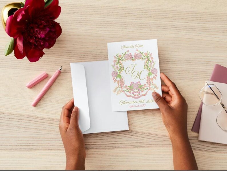May include: A white envelope with a floral save the date card. The card has a pink and green floral design with the initials "J & M" in gold script. The text "Save the Date" and "November 11th, 2023" is printed in gold script.