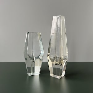 Könnte beinhalten: Zwei klare Glasvasen mit geometrischen Formen. Die größere Vase ist höher und hat eine größere Öffnung als die kleinere Vase.