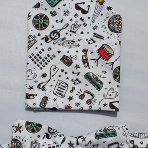 Puede incluir: Una pajarita y un pañuelo de bolsillo blancos con un tema musical. El patrón incluye notas musicales, instrumentos y otros iconos relacionados con la música.