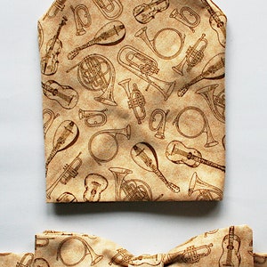 May include: A beige bow tie and pocket square with a brown musical instrument pattern. The pattern includes a variety of instruments, such as trumpets, french horns, and guitars.