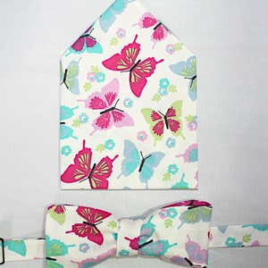 May include: A white bow tie and pocket square with a butterfly pattern in pink, blue and green.