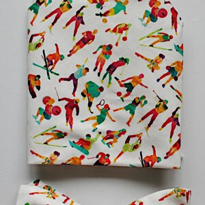 May include: A white bow tie and pocket square featuring a colourful pattern of people engaged in various sports. The design includes figures playing tennis, skiing, golf, and other sports.