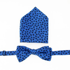 May include: A blue bow tie and pocket square set with a black leaf pattern.