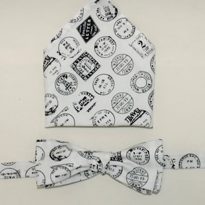 Puede incluir: Pajarita blanca con un patrón de sellos postales en blanco y negro. La pajarita está hecha de tela y tiene una forma clásica de pajarita.