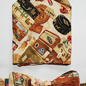 May include: A bow tie with a cream background and a pattern of vintage luggage, travel stickers, and stamps. The bow tie has a brown, red, and blue colour scheme.