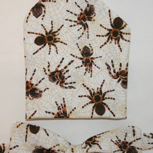 May include: A white bow tie and pocket square with a pattern of brown tarantulas on a web design.