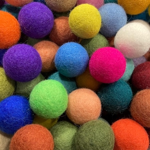 May include: A collection of colorful felt balls in various shades of blue, green, red, orange, purple, pink, and white. The balls are soft and fuzzy, and they are perfect for crafting or decorating.