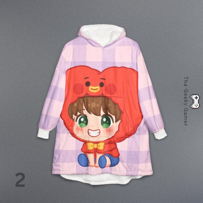 May include: A hooded blanket featuring a cartoon character design. The blanket has a pink and purple plaid pattern with a large graphic of a character with a red heart-shaped head and a smiling face. The Geeky Gamer logo is visible.