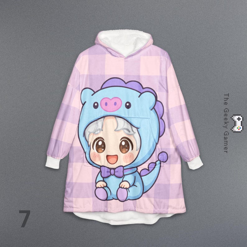 May include: A hooded blanket featuring a cartoon character in a blue dinosaur costume. The blanket has a pink and purple plaid pattern with white cuffs and a white-lined hood. The text "The Geeky Gamer" is visible.