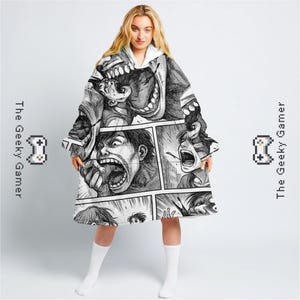 May include: A hooded blanket featuring a black and white manga-style comic print. The design showcases panels with screaming faces. The blanket has a white interior and is labeled with "The Geeky Gamer" and a pixelated controller graphic.