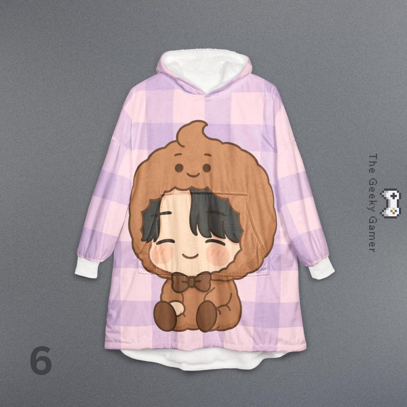 May include: A hooded blanket with a cartoon character design. The blanket features a large brown character with a smiling face and a bow tie, set against a pink and purple plaid pattern. The hood and cuffs are white.