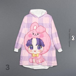 May include: A pink and purple plaid hooded blanket with a cartoon bunny design. The bunny has a pink hood, purple hair, and a yellow bow tie. The blanket has white cuffs and a white hood lining. The number "3" is in the bottom left corner.