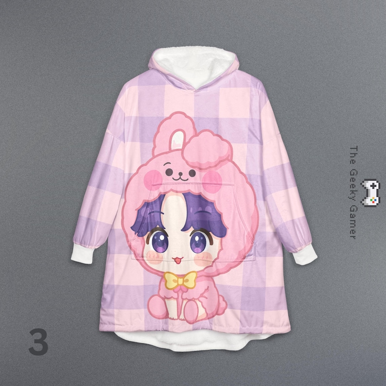 May include: A pink and purple plaid hooded blanket with a cartoon bunny design. The bunny has a pink hood, purple hair, and a yellow bow tie. The blanket has white cuffs and a white hood lining. The number "3" is in the bottom left corner.