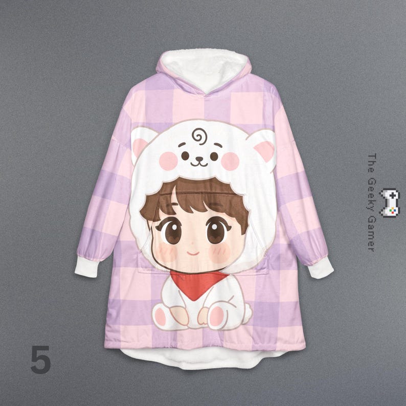 May include: A hooded blanket in a pink and purple plaid pattern, featuring a cartoon character with a bear-like hood. The character has brown hair, a red scarf, and a white bear hood with pink accents. The text "The Geeky Gamer" is on the right side.
