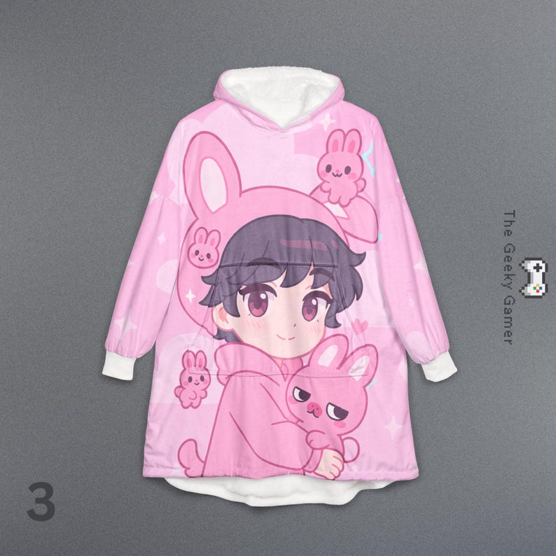 May include: Pink hooded blanket featuring an anime-style character wearing a bunny-eared hood and holding a plush bunny. The blanket has white cuffs and a white-lined hood. The Geeky Gamer logo is visible.