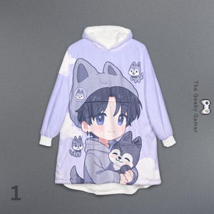 May include: A light purple hooded blanket featuring a cartoon illustration of a boy with blue eyes and a wolf hat, holding a wolf. The blanket has white cuffs and a white-lined hood. The text "The Geeky Gamer" is on the right side.