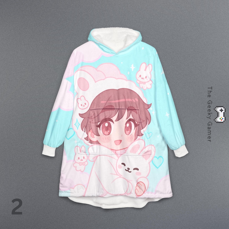 May include: A hooded blanket featuring a cartoon character with pink hair and a bunny hat, holding a bunny plush. The blanket has a light blue and pink color scheme with white cuffs and hood lining. The Geeky Gamer logo is visible.