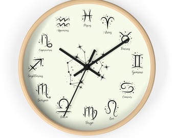 Puede incluir: Un reloj de pared redondo con marco de madera clara. La esfera del reloj es de color crema con símbolos del zodiaco negros y constelaciones de estrellas. Las manecillas negras indican la hora. El reloj mide aproximadamente 30 cm de diámetro.