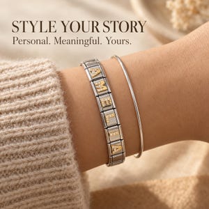 Op de afbeelding: Een zilverkleurige schakelarmband met goudkleurige letterbedels die AMELA spellen, elk versierd met kleine heldere steentjes, gecombineerd met een dunne, gladde zilverkleurige armband. De tekst STYLE YOUR STORY Personal. Meaningful. Yours. is zichtbaar.