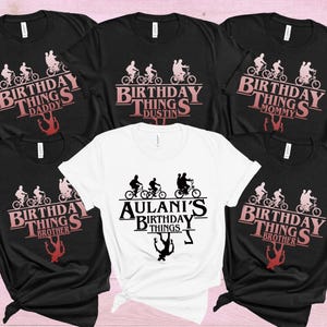 May include: A collection of black and white t-shirts with a birthday theme. The shirts feature a graphic of people riding bikes and the words "Birthday Things" with names like "Daddy," "Dustin," "Mommy," and "Brother." One white shirt says "Aulani's Birthday Things."