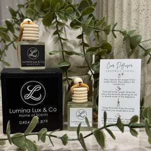 May include: A black box with the text "Lumina Lux & Co Home of Scents 0404 879" on it. A clear glass bottle with a wooden lid and a string attached to it. The bottle has the text "Lumina Lux & Co Home of Scents" on it. A white card with the text "Car Diffuser Instructions" on it. The card has instructions on how to use the car diffuser.