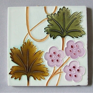 Può includere: Piastrella quadrata in ceramica con un motivo floreale. La piastrella presenta uno sfondo azzurro con un motivo di foglie e viti marroni e verdi. I fiori sono viola chiaro con centri viola scuro. La piastrella è quadrata e ha una superficie leggermente strutturata.