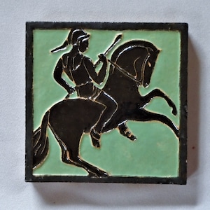 May include: Square ceramic tile with a black silhouette of a rider on a rearing horse. The background is light green, and the tile is framed with a dark border. The rider holds a spear, and the design has an antique aesthetic.