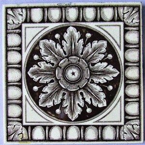 May include: A square ceramic tile featuring a dark brown and cream color palette. The center displays a detailed circular floral motif with radiating leaves. The border is decorated with a repeating pattern of oval shapes and corner leaf accents.