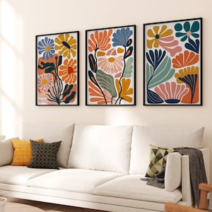 Könnte beinhalten: Drei gerahmte abstrakte Blumenprints im modernen, minimalistischen Stil. Die Drucke zeigen eine Vielzahl von Farben, darunter Orange, Pink, Blau, Grün und Gelb. Die Drucke sind in einer Reihe an einer weißen Wand angeordnet.
