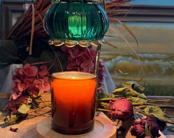 Puede incluir: Una lámpara calentadora de velas con un brazo metálico plateado curvado, una pantalla de vidrio estriado verde y una base redonda de madera clara. Un frasco de vela cilíndrico de vidrio con cera naranja se sitúa sobre la base.