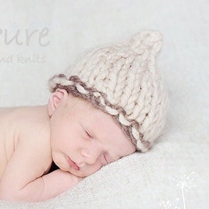 May include: A newborn baby wearing a cream knitted hat with a brown trim, sleeping on a white blanket. The hat is hand-knitted and the image includes the text "Pure hand knits" and "hazel irvine PHOTOGRAPHY".