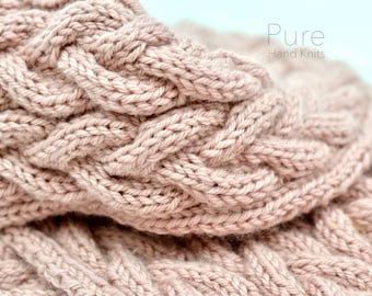 May include: Close-up of a soft, pink knitted scarf with a cable knit pattern. The scarf is made with a fine yarn and has a delicate texture.