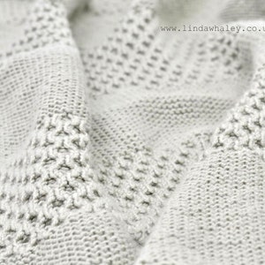 May include: Close-up of a white knitted blanket with a textured pattern. The blanket is soft and fluffy, and the texture is visible in the image.